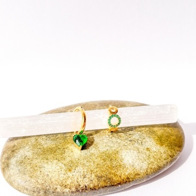 Anéis dourados com pendentes verdes sobre pedra lisa