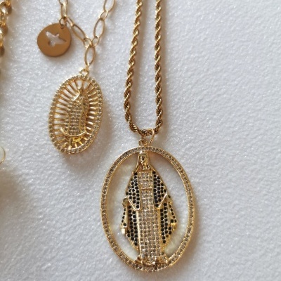 Colares dourados com pendentes ovais detalhados em preto, branco e dourado sobre fundo branco.