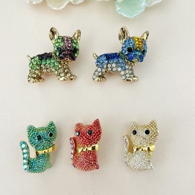 Pins de cães e gatos com strass coloridos e detalhes dourados sobre fundo claro com flores decorativas.