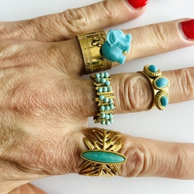 Mão com anéis dourados e turquesa em fundo branco com acessório azul