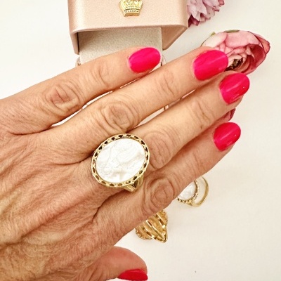 Mão feminina com anel dourado e pedra branca com caixa rosa e flores rosas