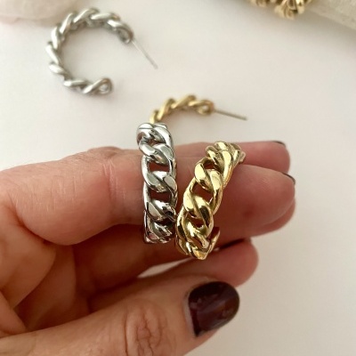 Brincos de aro em metal trançado prateado e dourado sobre fundo claro com mão segurando dois pares.