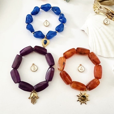 Três pulseiras de contas coloridas com pendentes dourados em fundo branco