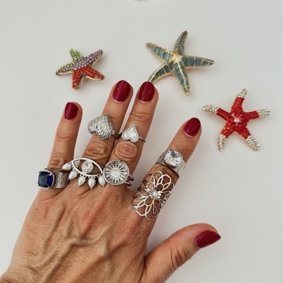 Mão com anéis variados e estrelas-do-mar decorativas no fundo branco.
