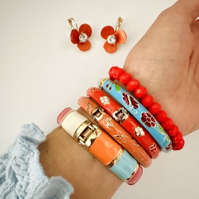 Pulseiras coloridas com padrões florais dourados usadas num pulso, com brincos vermelhos no fundo.