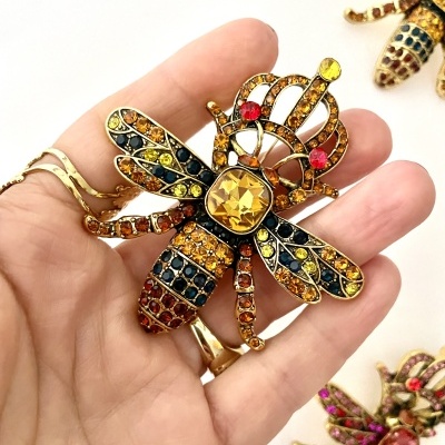 Broche em forma de abelha colorida com pedras brilhantes numa mão