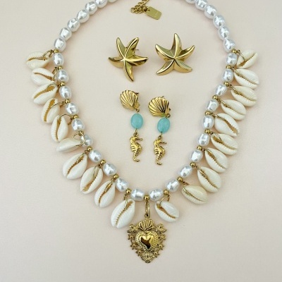 Conjunto de colar com pérolas, búzios e pingente dourado, com dois pares de brincos dourados e azul sobre fundo bege.