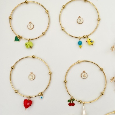 Quatro pulseiras douradas com pingentes coloridos diferentes sobre fundo branco