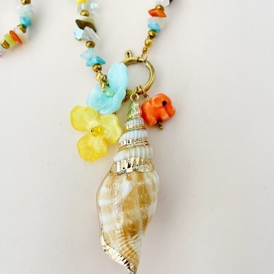 Colar com conta concha dourada, flor amarela e peixe laranja sobre fundo branco.