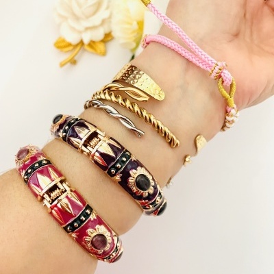 Pulseiras coloridas e douradas no pulso com flores decorativas ao fundo