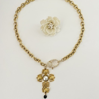 Colar dourado com pendente de cruz e broche floral branco com pérolas