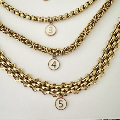 Três pulseiras douradas com pendentes numerados 3, 4 e 5 sobre fundo branco