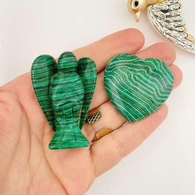 Pedras malachite em forma de anjo e coração na mão com pássaro dourado em fundo branco