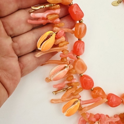Colar colorido com coral, conchas e contas douradas na mão