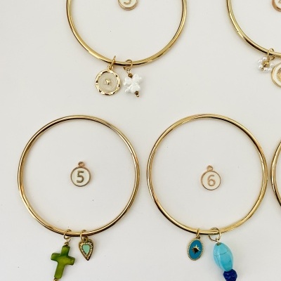 Pulseiras douradas com pendentes variados e etiquetas numeradas em fundo branco