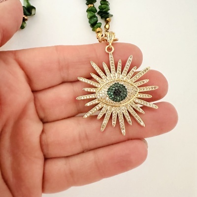 Colar com pendente de olho em metal dourado com pedras verdes e transparentes em fundo branco
