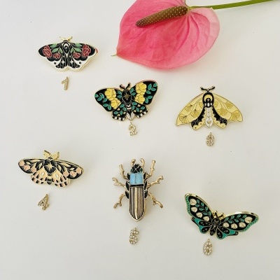 Pins esmaltados de insetos coloridos numerados 1 a 5 ao lado de flor rosa