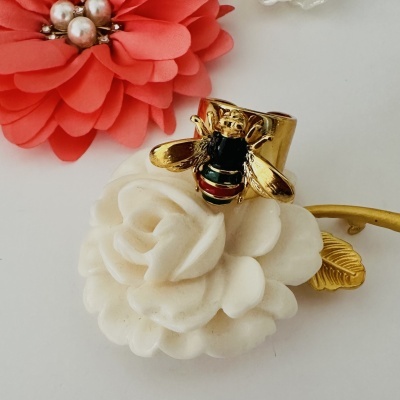 Anel dourado com abelha esmaltada sobre flor branca, flor vermelha de tecido ao lado