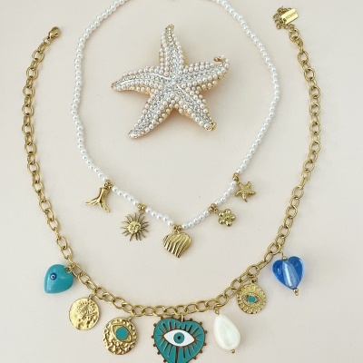 Dois colares com pingentes coloridos e um broche estrela-do-mar de pérolas sobre fundo claro.