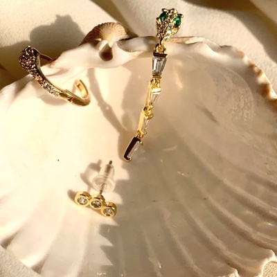 Brincos dourados com pedras dentro de concha branca sobre tecido bege