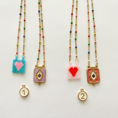 Dois colares com contas coloridas e pendentes de coração, junto com pendentes redondos numerados 1 e 2, em fundo branco