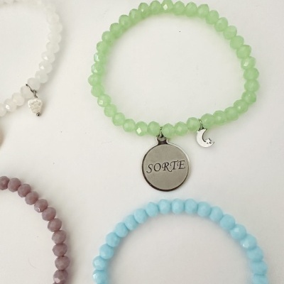 Pulseiras coloridas de contas facetadas com pendentes metálicos e a palavra SORTE