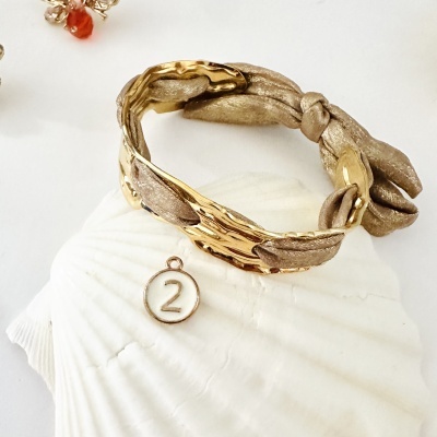 Pulseira dourada com tecido e medalhão branco com número 2 sobre concha