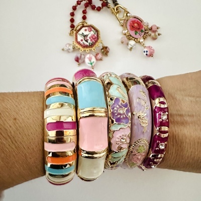 Pulseiras coloridas com detalhes dourados e esmaltados num pulso, com pendentes florais ao fundo