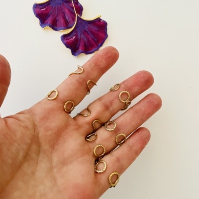 Brincos roxos e dourados pendentes e anéis dourados sobre mão humana