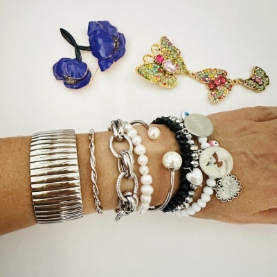 Pulseiras variadas de metal e contas com presilha de flor azul e broche de borboleta colorida sobre fundo branco.