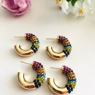 Dois pares de brincos argola dourados com pedras coloridas e flores ao fundo.