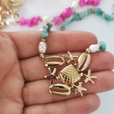 Colar dourado com conchas e estrelas do mar, pedras azuis e pérolas numa mão