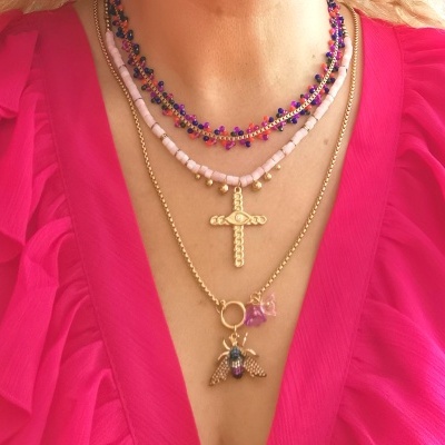 Quatro colares dourados e coloridos usados sobre blusa rosa vibrante com folhos