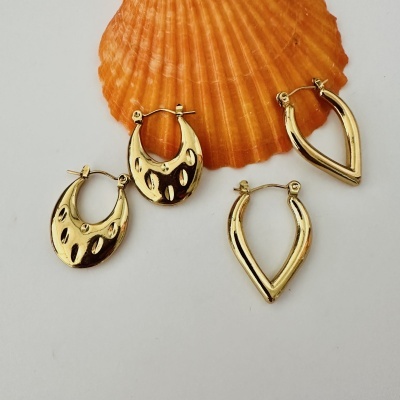 Quatro pares de brincos dourados diferentes sobre fundo branco com concha laranja