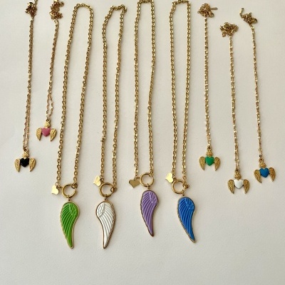 Conjunto de brincos e colares dourados com pendentes coloridos em forma de asa e coração sobre fundo branco.