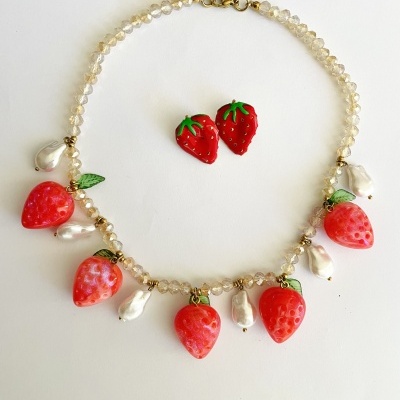 Conjunto de colar com pendentes de morangos e pérolas falsas com brincos de morangos sobre fundo branco