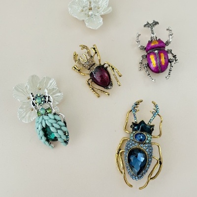 Broches de insetos com pedras coloridas e flores brancas