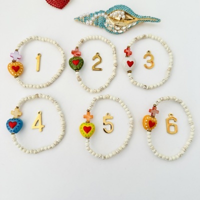 Pulseiras com contas brancas e corações coloridos, com números dourados, broche concha com pérolas e pedras azuis