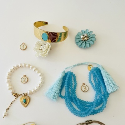 Cinco peças de bijuteria numeradas sobre fundo branco, incluindo pulseiras, colares e flores de tecido.