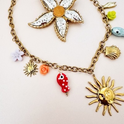 Colar dourado com vários pendentes coloridos sobre fundo claro