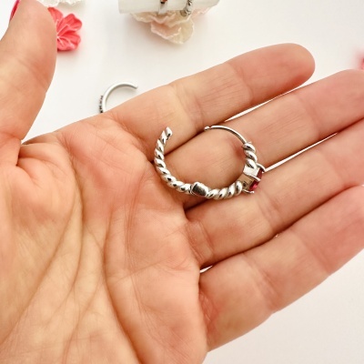 Argola de brinco prateada com padrão torcido na mão sobre fundo branco com flores