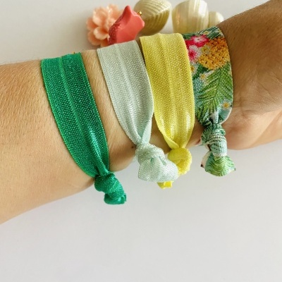 Pulseiras elásticas coloridas no pulso com conchas decorativas ao fundo