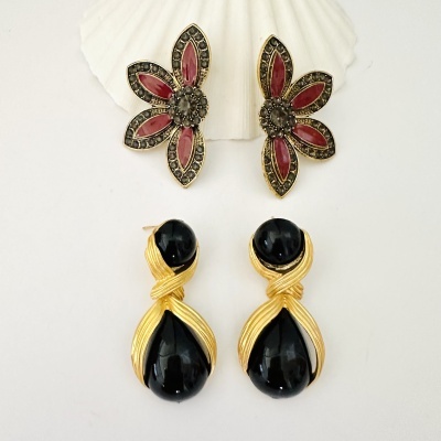 Dois pares de brincos, um floral vermelho e preto, outro com pedras pretas e metal dourado.