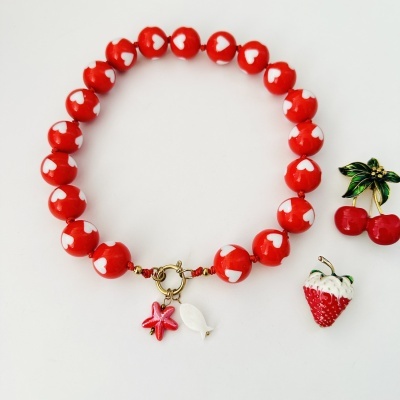 Colar com bolas vermelhas decoradas com corações brancos e vários pendentes coloridos sobre fundo branco.