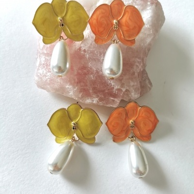Quatro brincos florais de resina amarela e laranja com pérolas brancas, sobre cristal rosa