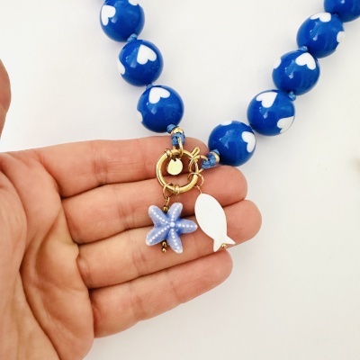 Colar azul com corações brancos e pendentes marinhos a ser segurado por uma mão