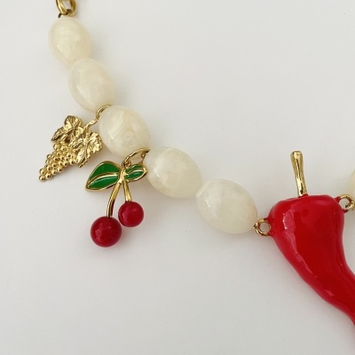 Pulseira com contas brancas e pendentes de cachos de uva dourados, cerejas vermelhas e pimento vermelho