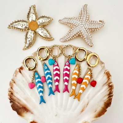 Brincos e broches com formas de peixes e estrelas do mar sobre uma concha