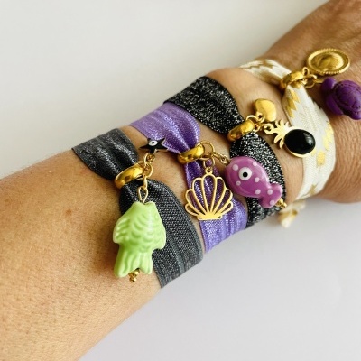 Pulseiras coloridas de tecido com pendentes em braço sobre fundo branco.