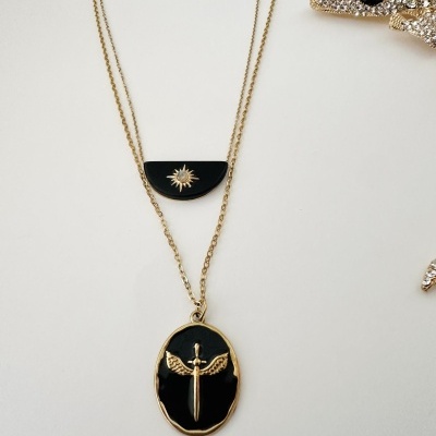 Colar com dois pendentes negros com detalhes dourados sobre fundo branco.